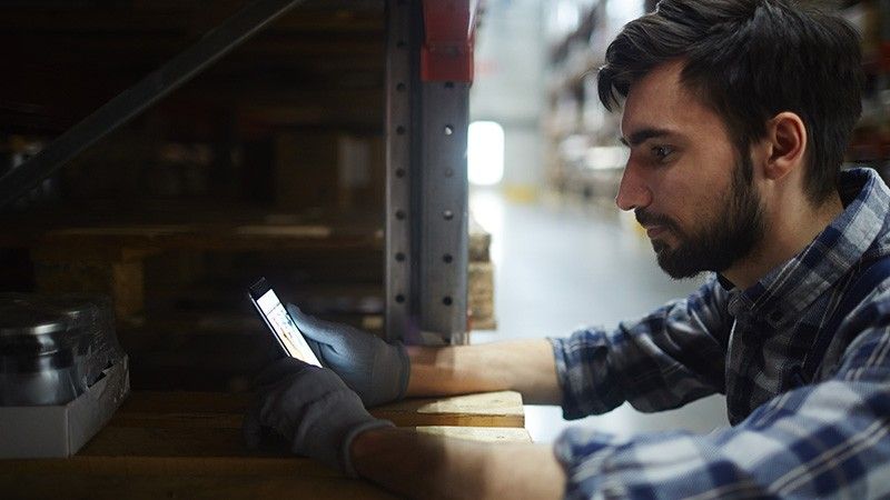 man in warehouse looks at smart phone