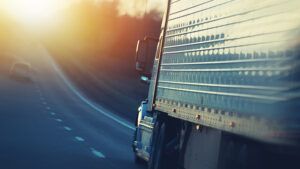 Side of a truck driving down the highway, into the sunset.