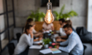 Team meeting in the background with a lightbulb in the foreground