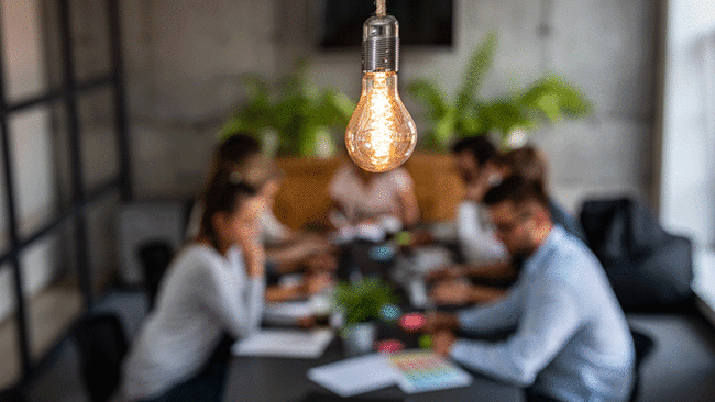 Team meeting in the background with a lightbulb in the foreground