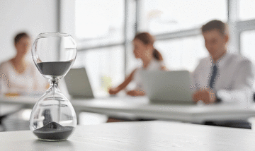 Hourglass on a table with corporate workers in the background